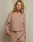 A woman with wavy blonde hair wears the Perfectwhitetee Cami Terry Stripe LS, an oversized beige and red striped top with matching drawstring shorts, standing before a plain light-colored fabric backdrop.