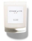 A 14 OZ Classic Highball soy coconut blend candle by Voyage Et Cie, in a clear jar labeled "VOYAGE ET CIE est. 2005" and "VAL D’ISERE LES PINEEDS," sits unlit, casting a soft shadow to the right.