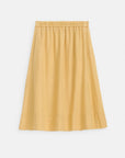 The Alex Mill Maddie Skirt Linen is a knee-length, A-line linen skirt in light mustard yellow with an elastic waistband, seam details, and pockets; garment-dyed for a textured look—shown on a white background.