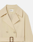 Close-up of The Uniform Trench by FRAME—a lightweight beige coat featuring wide lapels, double-breasted buttons, a matching belt with a rectangular buckle, and the FRAME label inside the collar.
