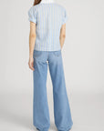 A person stands with their back to the camera, wearing FRAME’s The Boardwalk Shirt in a relaxed fit with white and yellow stripes, paired with high-waisted, wide-leg blue jeans. The background is plain white.
