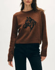 A woman wears the White + Warren Horse Embroidered Crew, a brown Western sweater featuring a hand-embroidered black horse's head on the front, paired with black pants against a plain light background.