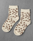 A pair of Unified Leopard Socks in cream with brown animal prints, laid flat on a textured gray surface.