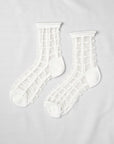 Unified’s Sheer French Window socks feature a white grid pattern on see-through fabric with solid white toes, heels, and cuffs for an airy look. Shown laid flat on a white surface.