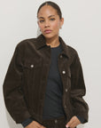 A person with pulled-back hair wears the Alex Mill Camden Rider Jacket in corduroy over a black top, standing against a plain white background with a neutral expression.