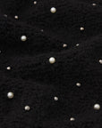 A detailed view of FRAME’s The Embellished Jacket, featuring textured black knit fabric adorned with scattered small and large white pearls.