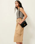 A woman stands sideways against a plain backdrop, wearing a sleeveless black-and-white checkered crop top, Sessun Marco Bermuda Shorts in gabardine twill with large pockets, and carrying a black shoulder bag.