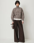 Sessun Orozco pleated large pants with a chunky knit turtleneck, styled by a white wall for a relaxed look.
