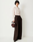 Sessun Orozco Large Pleat Pants styled with a pale pink shirt, shown with a burgundy handbag by a white wall.