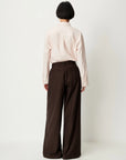 Sessun Orozco pleated large pants and light shirt, model facing away, relaxed modern style.