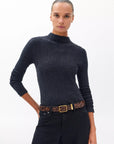 A woman with slicked-back hair wears a textured black long-sleeve top, black jeans, and the Rag & Bone X Boyfriend Belt, standing against a plain white background.