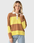 A blonde woman wears the Xirena Braxton Sweater—brown and yellow stripes with a white collar—styled with blue jeans, against a light background.