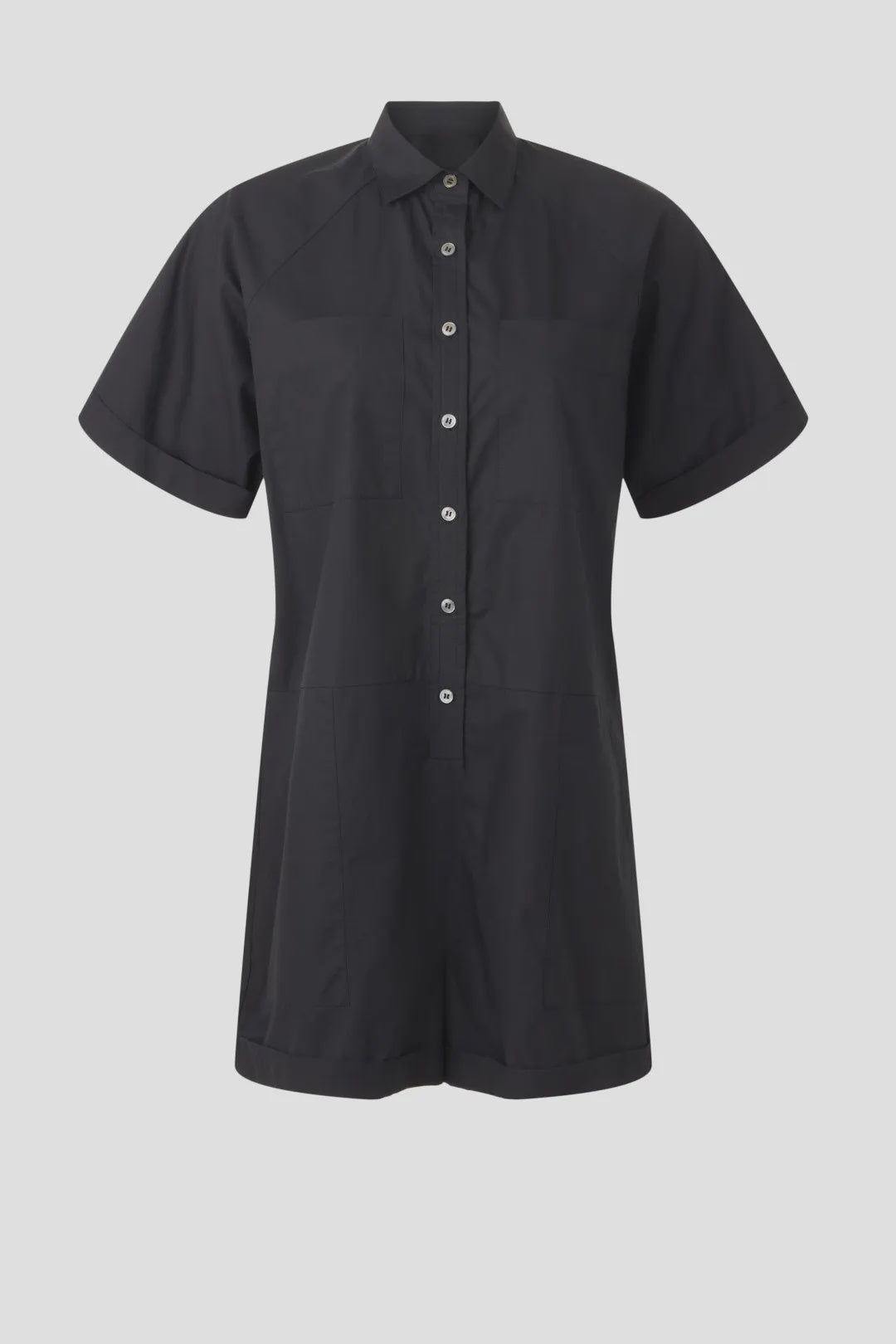The Franklin Romper by Xirena is a black, short-sleeved, button-up romper with a collar, front patch pockets, and a relaxed utility fit, shown against a plain light gray background.