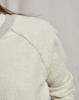 Close-up of a person wearing the Perfectwhitetee Ziggy Reverse LS Sweatshirt in off-white cotton fleece with a light gray collar and seam details; only the shoulder, part of the arm, and some hair show against a neutral background.