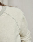 Close-up of a person wearing the Perfectwhitetee Ziggy Reverse LS Sweatshirt in off-white cotton fleece with a light gray collar and seam details; only the shoulder, part of the arm, and some hair show against a neutral background.