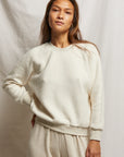 Someone with long hair wears a Ziggy Reverse Fleece LS Crew Sweatshirt from Perfectwhitetee and matching pants, standing against a plain backdrop. They have a relaxed expression, with one hand on their hip.