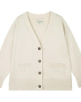 The Boyfriend Heavy Cardigan by Jumper 1 2 3 4/CR2 is a cream cashmere knit with an oversized fit, long sleeves, two front pockets, ribbed cuffs and hem, and a V-neckline with four brown buttons.