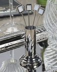 The Zodax Cocktail Picks S4 features four silver picks with square white tops in a matching holder, elegantly displayed on a reflective tray—an ideal sleek accent for your modern barware collection.