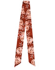 The Rustic Wild Rose Twilly Scarf by Faire is a long, narrow silk accessory with pointed ends, showcasing a hand-drawn pink rose and leaf design on a reddish-brown background.