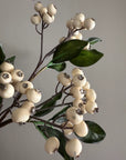 Faux cream berry and green leaf pick by Faire, 15-inch stem against a gray background.