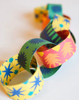 The Faire Paper Garland/Chains feature interlocking loops with vibrant starburst and sunburst patterns in yellow, green, blue, and red—perfect for festive birthday decorations or garlands, beautifully displayed on a white surface.