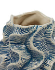 A close-up of the Bloomingville Textured Vase, showcasing its wavy edges and blue leaf-like patterns on a white surface. This handcrafted piece features an uneven, organic opening at the top.