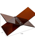 The Bloomingville Acrylic Book Holder is an amber, X-shaped stand made of glossy acrylic panels, measuring 3.5" tall, 6" wide, and 11.5" long—perfect for elegantly displaying books.