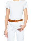 Dressed in a white t-shirt and jeans, a person poses with one hand on their waist, flaunting Jerome Dreyfuss's Festival Ceinture — a chic tan cowskin leather belt embellished with gold studs and a shiny gold buckle, while their other arm hangs relaxed by their side.