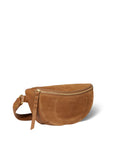 A tan suede Lino Banana bag by Jerome Dreyfuss, featuring a zippered top and matching adjustable strap, lies on a plain white background. The handmade bag is adorned with a decorative tassel on the side.
