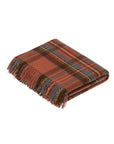 The Faire BM Merino Lamb Throw/Blanket features a folded, fringed tartan design in rust, blue, brown, and beige, crafted from soft Merino Lambswool and inspired by traditional clan patterns.