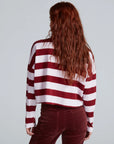 A person with long, wavy auburn hair is seen from behind, wearing the ASKK Cropped LS Tee in red and white stripes and dark red corduroy pants, set against a plain light gray background.