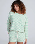 A person with curly hair wears the ASKK Easy Pull Over, a relaxed 100% cotton long-sleeve top with green stripes and a front pocket, paired with matching shorts, made in Los Angeles, against a plain light background.