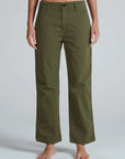A person stands barefoot, wearing ASKK's Tomboy Chino—high waist, straight-leg olive green pants made from stretchy twill. The waist-down shot highlights these mid weight chinos against a plain light gray background.