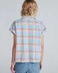 A person with short, wavy blonde hair is shown from the back, wearing the ASKK Virginia Shirt—a relaxed short-sleeve button-up plaid made of lightweight cotton—paired with light blue jeans.