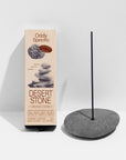 A box of Faire Low Smoke Incense stands next to a lit stick in a smooth gray stone holder against a white background. The beige packaging features stone graphics and product details.