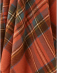 A close-up of Faire's BM Merino Lamb Throw/Blanket reveals its soft Merino lambswool texture, featuring orange, blue, yellow, and brown plaid with diagonal folds and classic clan checkered lines.