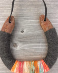 The Lucky Horseshoe by Faire features upcycled horseshoes wrapped in dark gray and multicolored yarn with orange, pink, yellow, and teal accents. Hung by a black cord, this unique piece makes a personalized gift.