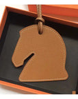 The Faire Bag Charm, a brown leather horse head accessory, comes in an orange and black gift box—perfect for adding a unique, personal touch to your handbag.