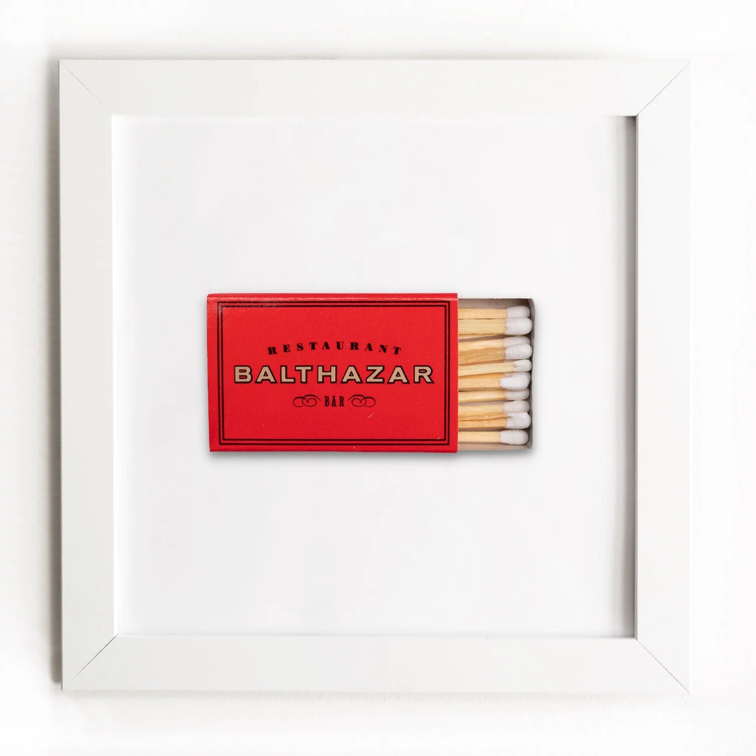 A framed display featuring a red matchbook from Restaurant Balthazar with Arizona style, alongside a row of matches, all against an Art Square White Frame background by Match South.