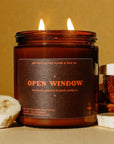 The Faire Banana Nut Bread Candle, labeled "OPEN WINDOW" and featuring banana, brown sugar, and vanilla notes, sits beside banana slices and banana bread on a beige background.