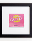 A framed picture displays a pink square matchbook centered against a white background. The matchbook features the words "California Dream Barbie" in yellow and white lettering on the front. The minimalist design is enhanced by the clear acrylic frame, adding a modern touch to this Match South Art Square Blk Frame art print.