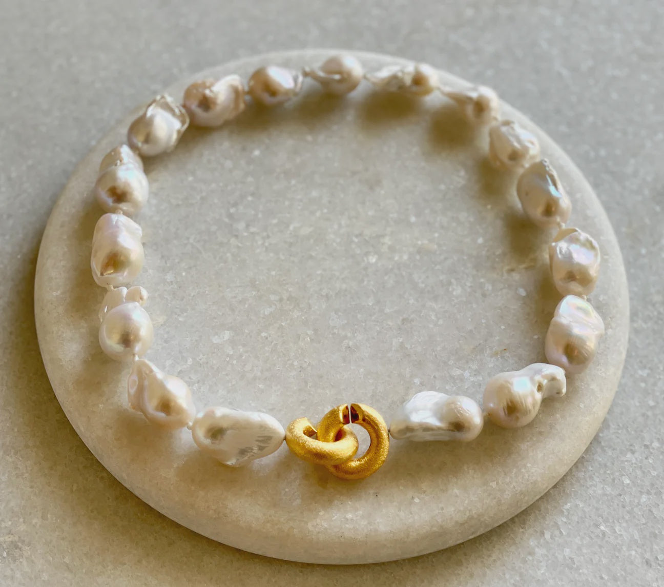 Bittersweet Designs Short Baroque Pearl Necklace with Gold Clasp displayed on a round, flat stone surface, featuring a unique gold clasp at the center in Arizona style.