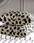 Two PARK AVE ANIMAL chenille pillows by Eastern Accents, featuring a beige and black leopard print, are stacked on a bed with white and black striped bedding, adding a chic animal print accent to the room.
