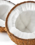 Two halves of a brown coconut with white flesh are shown on a white background, highlighting the natural source of Faire Monoi Coco Coconut Oil. The rough shell and smooth interior illustrate its pure, nourishing origin.