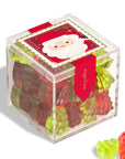 A clear plastic Christmas Candy Cube by Faire, filled with red and green tree-shaped candies, features a festive Santa label on top and a red "sugarfina" ribbon on the side. Two gummies are displayed outside the box.