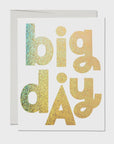 A Faire greeting card with the phrase "big day" in large, bold, glittery letters in various shades of gold and green, displayed against a plain white background at a bungalow.