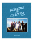 The "Blondie In Camera 1978" book cover from Simon & Schuster Inc. features a blue background, the title above a classic rooftop photo of Debbie Harry and Blondie, and Martyn Goddard’s name at the bottom.
