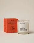A glass "Below 60 Candle" by Faire stands beside its orange box, both labeled with “BRIGHTER THAN A BLOOD ORANGE MOON” and an orange illustration. This Leaping Bunny certified soy wax candle has a fresh orange & ginger scent.