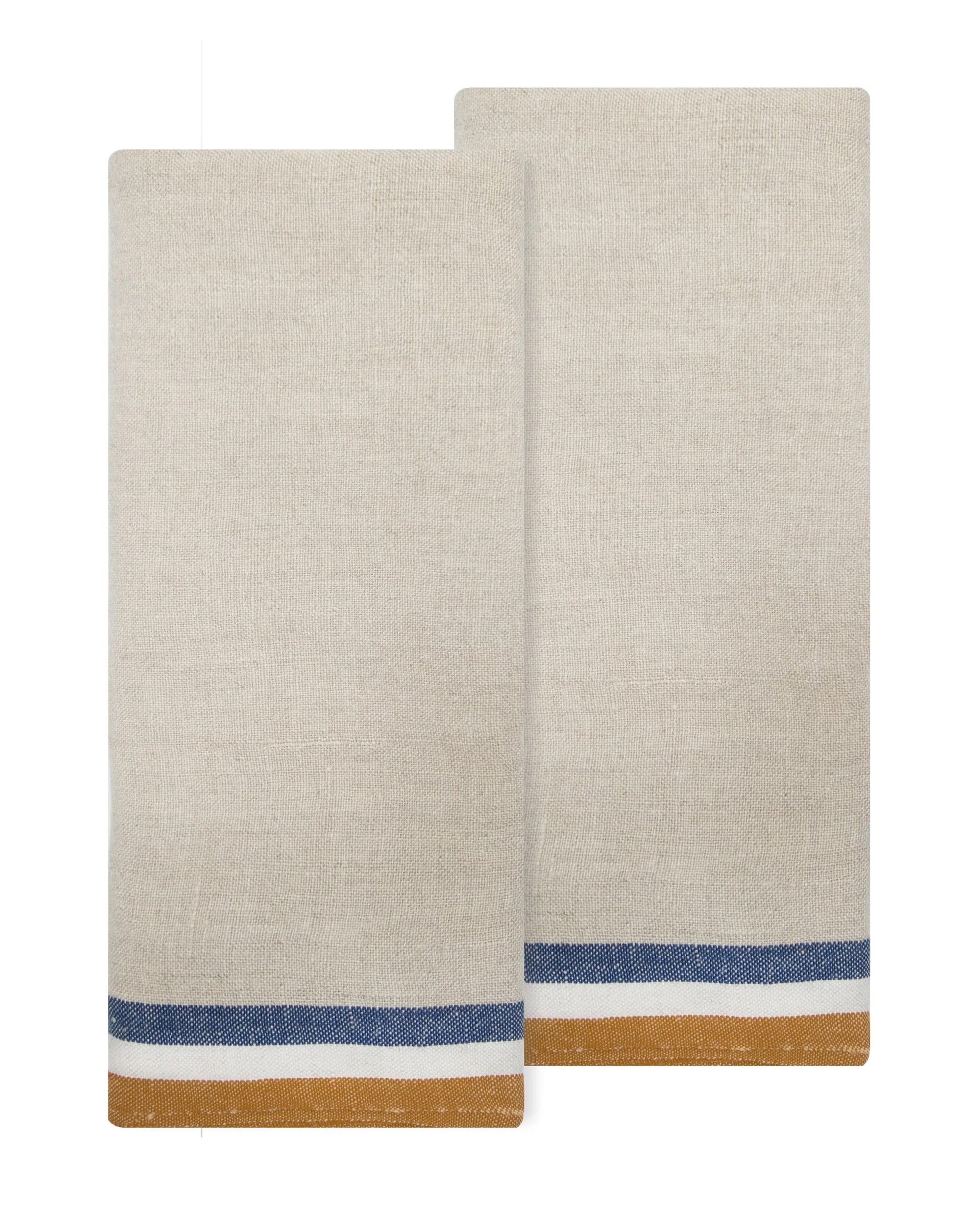 The Caravan Normandy Natural Towel Set-2 features two beige cloth napkins with blue and mustard yellow borders, inspired by classic French kitchen towels. They are shown slightly overlapping for an elegant, timeless appeal.