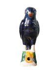 The Parrot Small by Blue Ocean Traders is a ceramic bird whistle shaped and painted like a dark blue bird with an orange beak, perched on a green and white base, inspired by Jingdezhen hand-painted porcelain craftsmanship.
